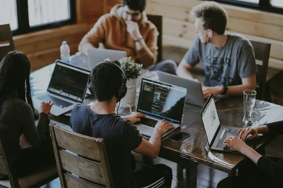Coworkers collaborate around a table with laptops and notebooks.