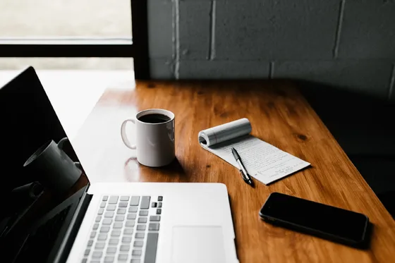 A notebook, laptop, phone, and coffee are arranged on a desk.