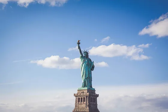 The Statue of Liberty stands against a bright blue sky.