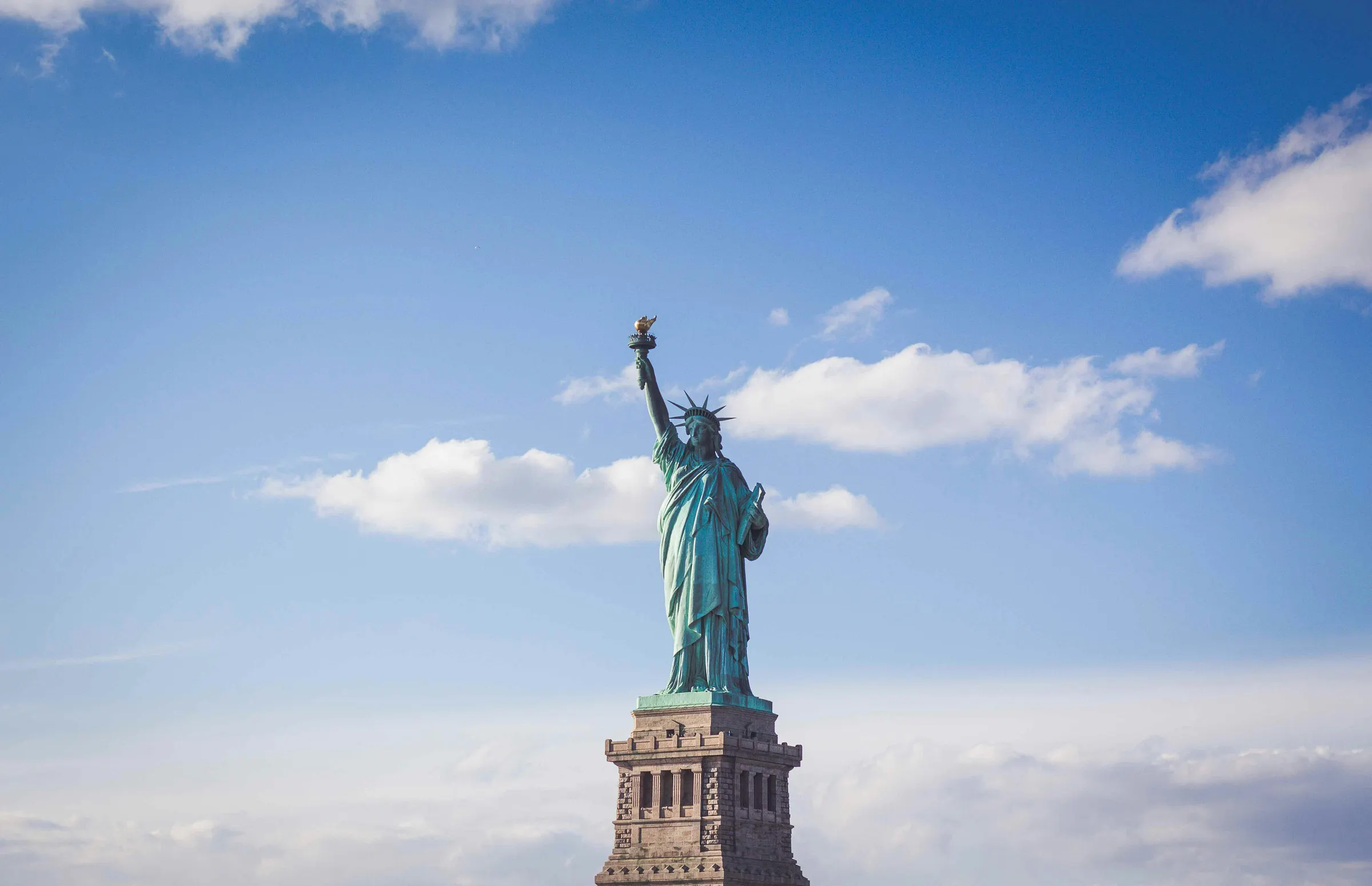 The Statue of Liberty stands against a bright blue sky.