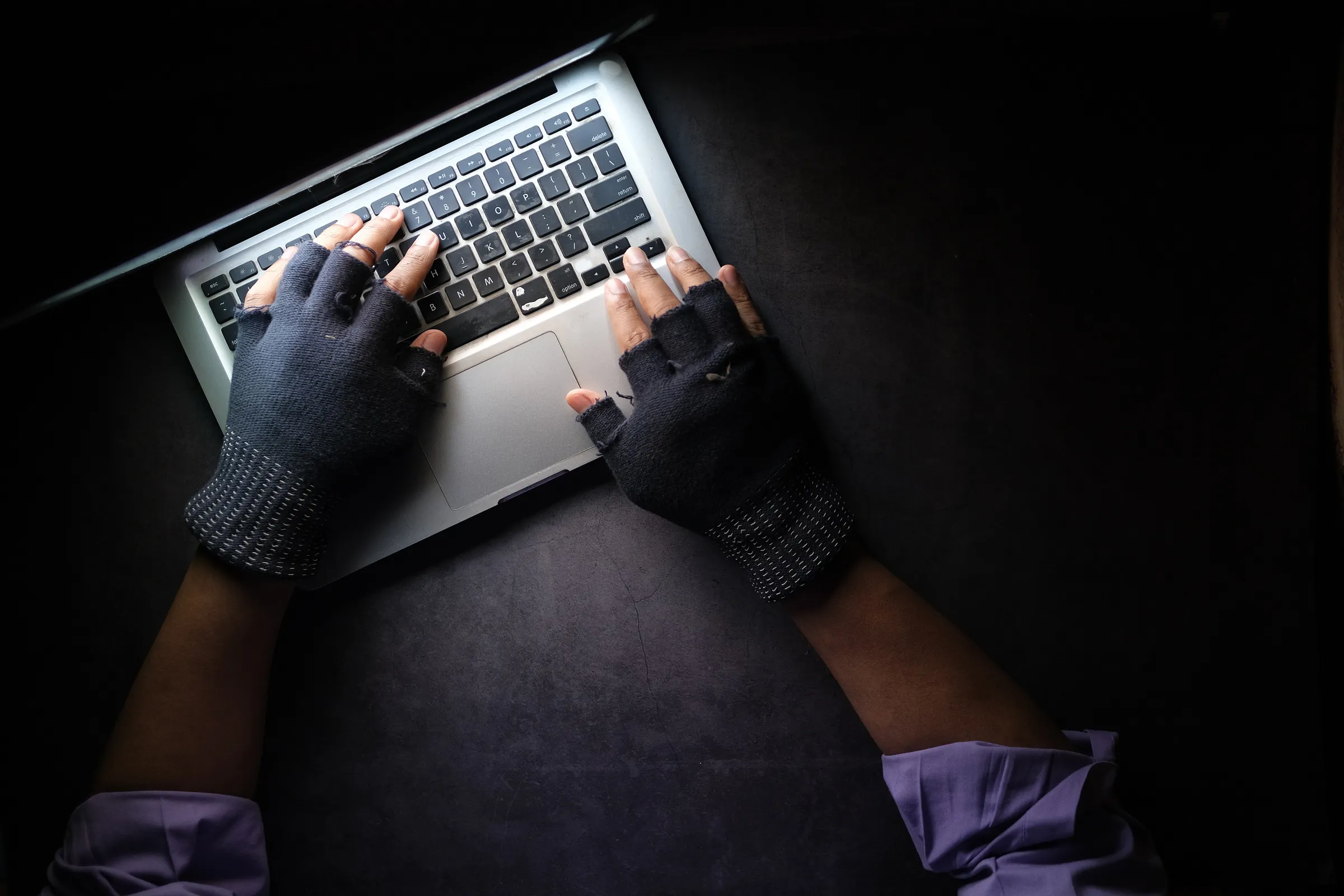 A person wearing black gloves types on a laptop.