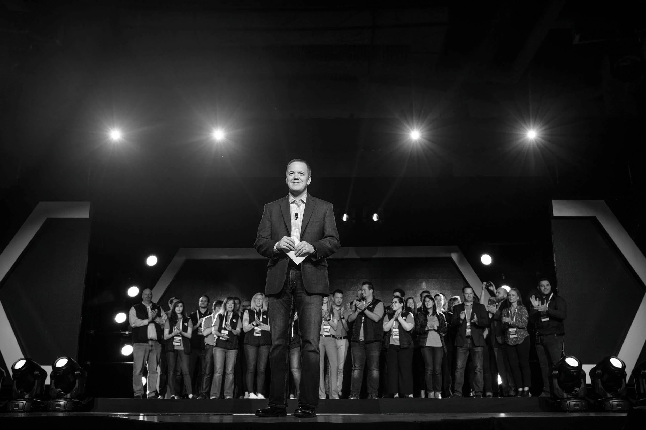 Aaron Klein speaking on a dark stage under spotlights.
