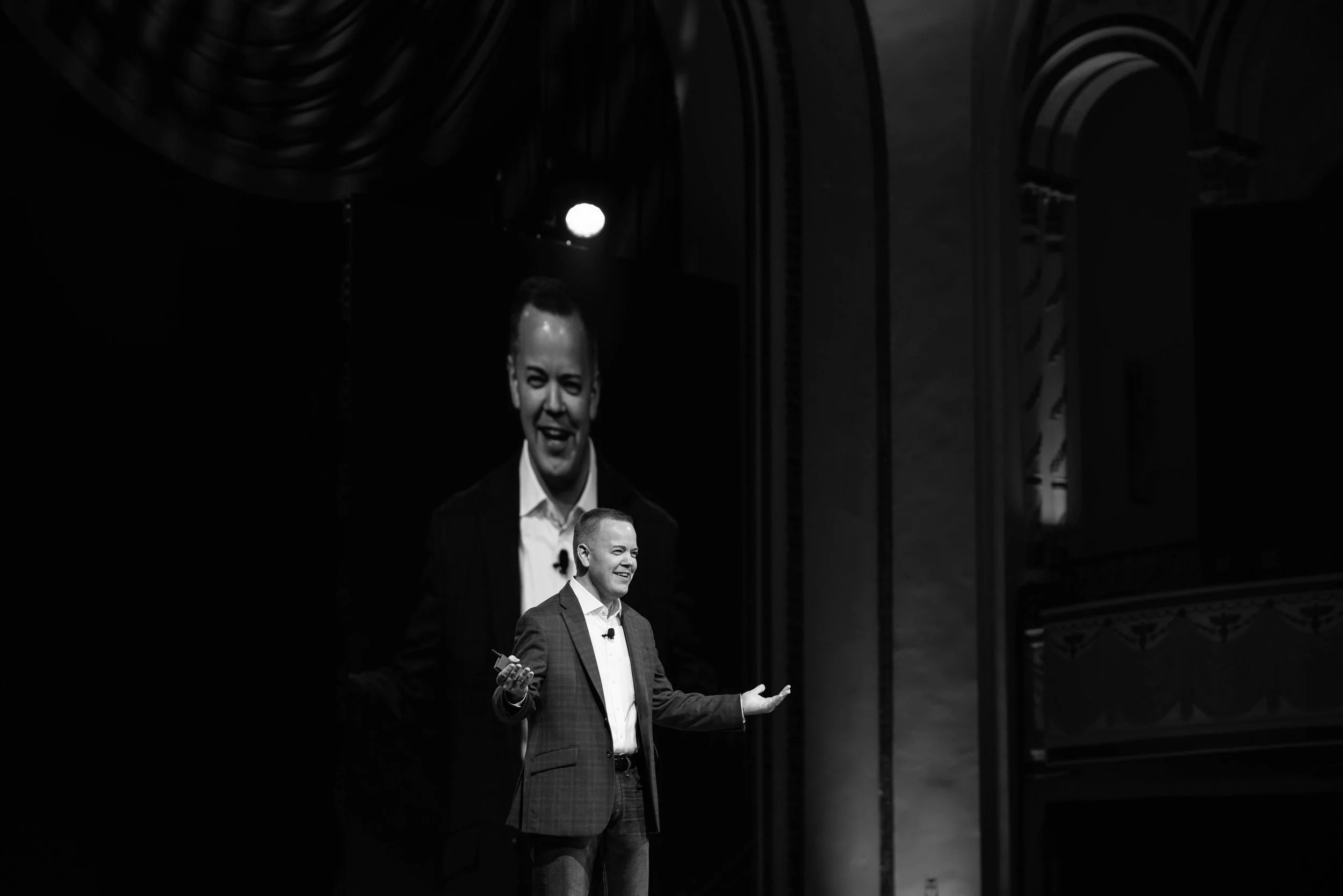 Aaron Klein speaking onstage beneath a large projected image of himself.